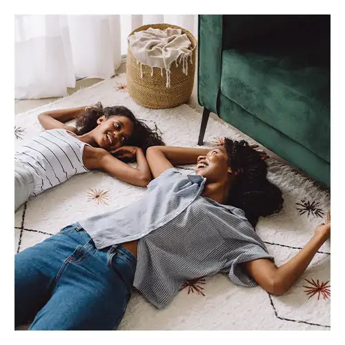 Two people relaxing on a white wool rug with colorful accents in a cozy living room, symbolizing comfort and long-lasting quality