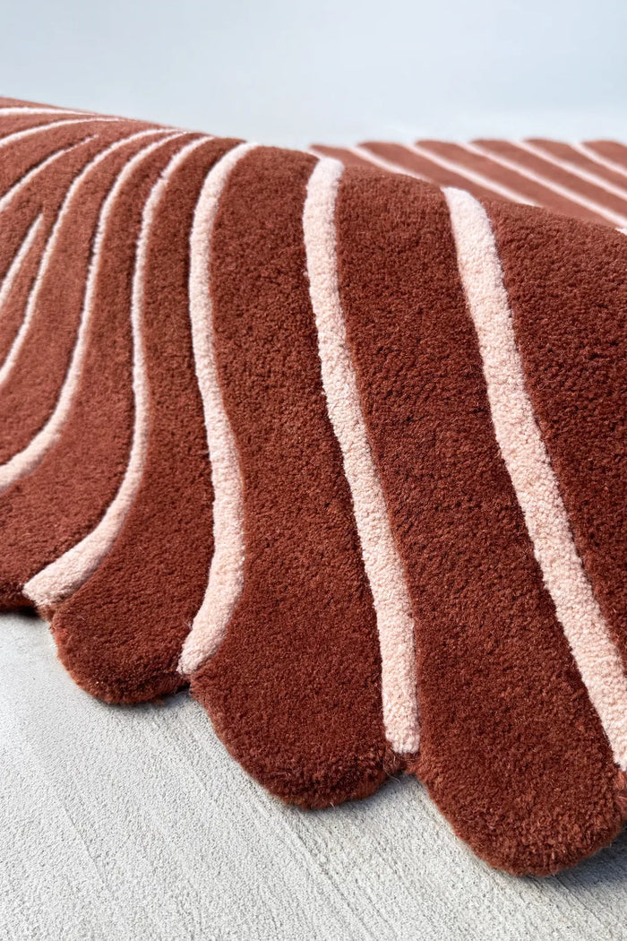 Close-up of sculpted wool rug edge showing scalloped rust border and cream stripe carving