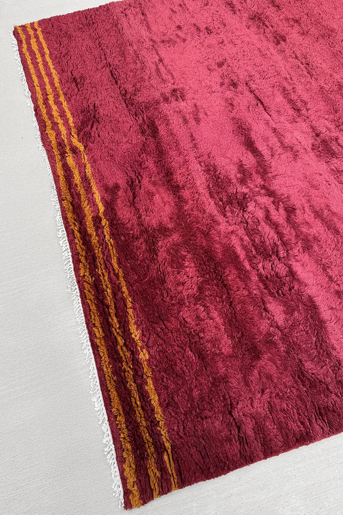 Red and yellow striped shag rug with hand-knotted fringe, shown at an angle to highlight high-pile wool texture