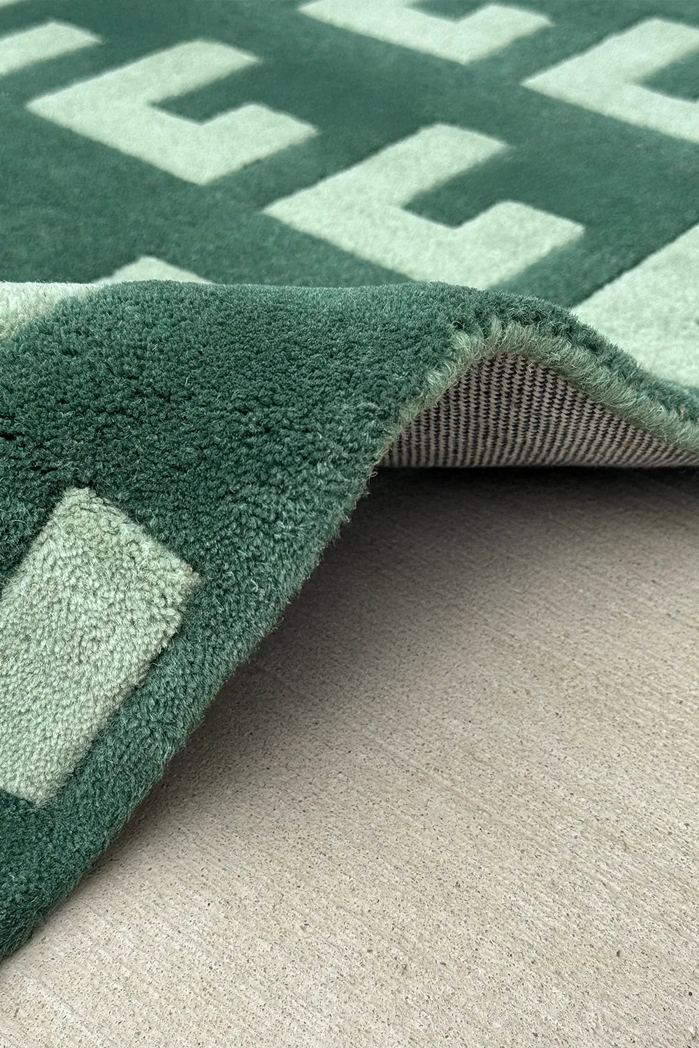Rolled view showing edge finishing of modern green wool rug

