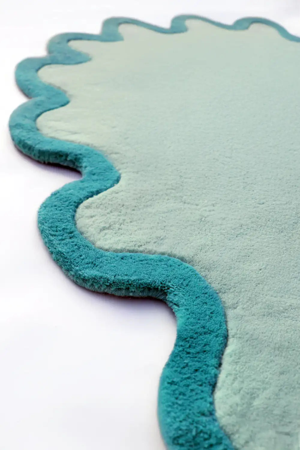 A close-up of the scalloped edge on a hand-tufted teal wool rug, showing its wavy form and plush pile