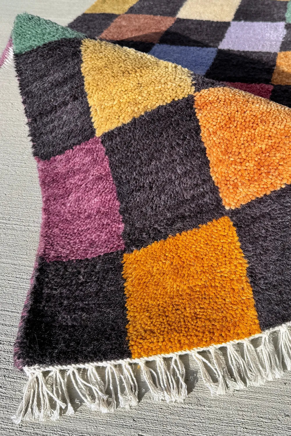 Handmade wool rug featuring a vibrant checkerboard pattern with mustard, burnt orange, sage, lilac, red, and blue squares.