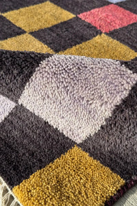 Black and multicolor wool rug with mustard, burnt orange, sage, red, and blue checkered squares.