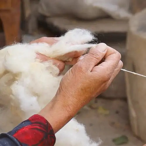 Hands spinning high-quality natural wool fibers by hand, showcasing the artisanal craftsmanship behind every Jubi Rug.