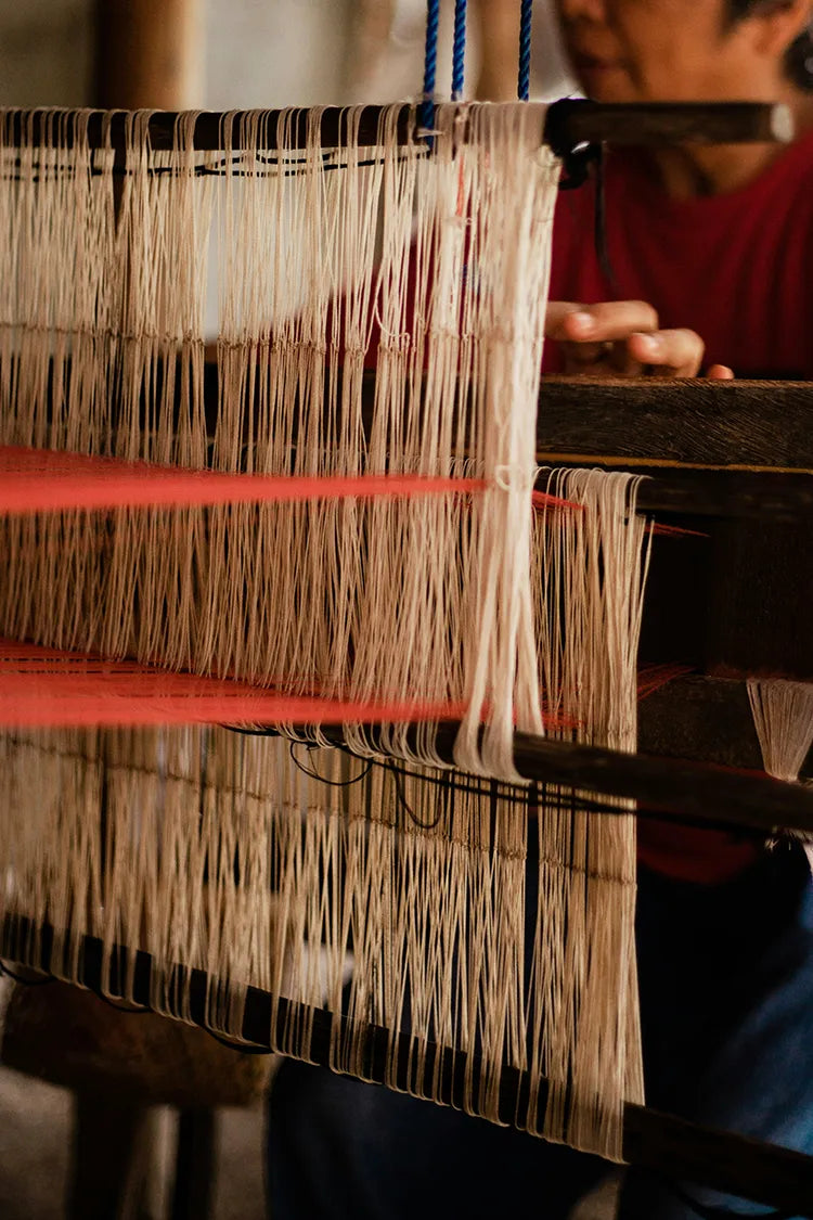 Close-up of an artisan weaving threads on a traditional handloom, showcasing the intricate craftsmanship behind Jubi rugs.