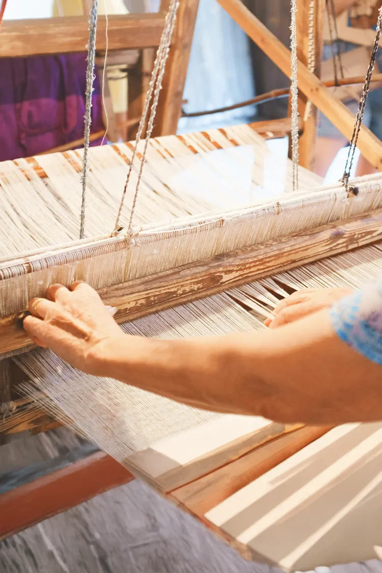 A close-up of a traditional wooden loom in use, with skilled hands weaving a rug using natural materials