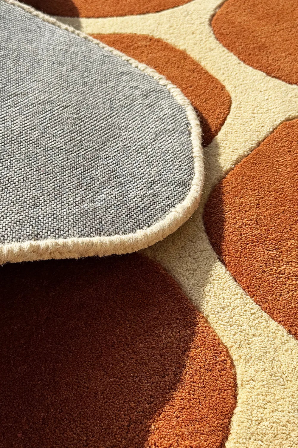 Close-up of tufted wool rug with cream border and terracotta tone – irregular shape rug with soft sculpted details