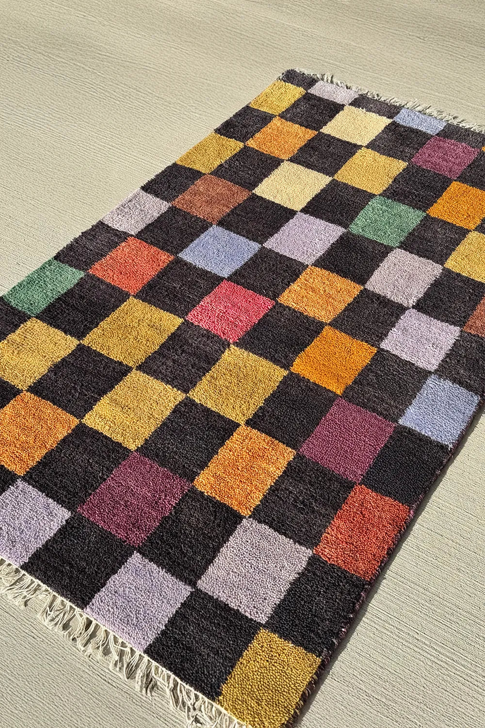 Colorful checkered area rug with mustard yellow, burnt orange, sage green, and lilac squares.