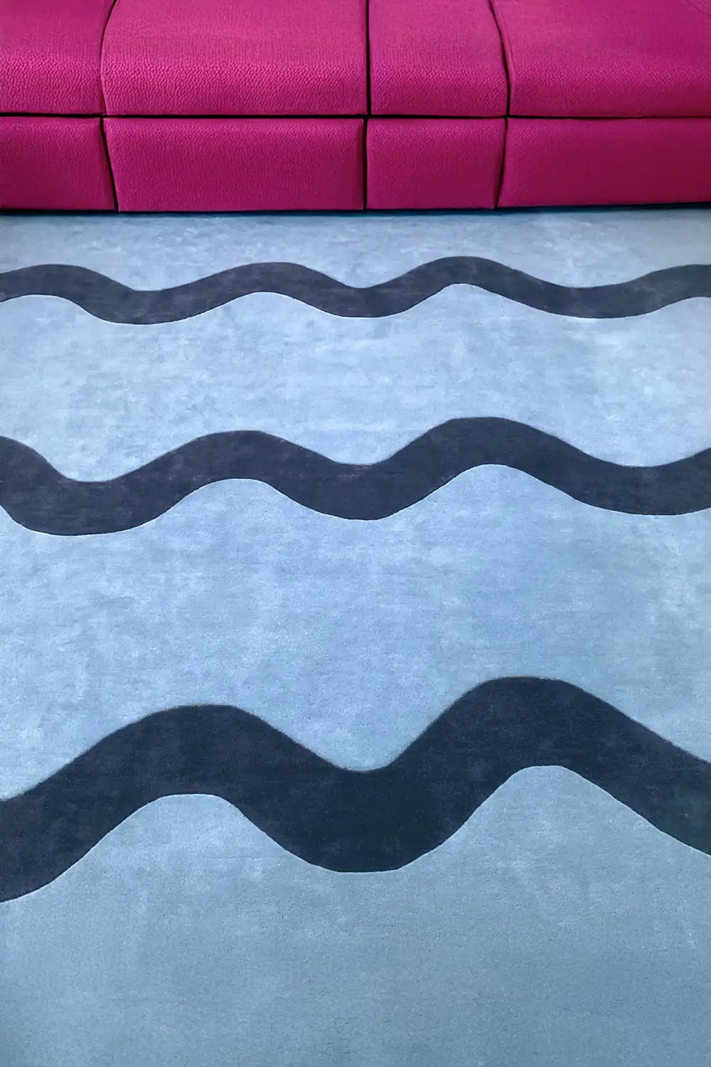 jubi light blue square wool area rug with dark blue unique wavy stripe in a modern living room with a dark pink couch