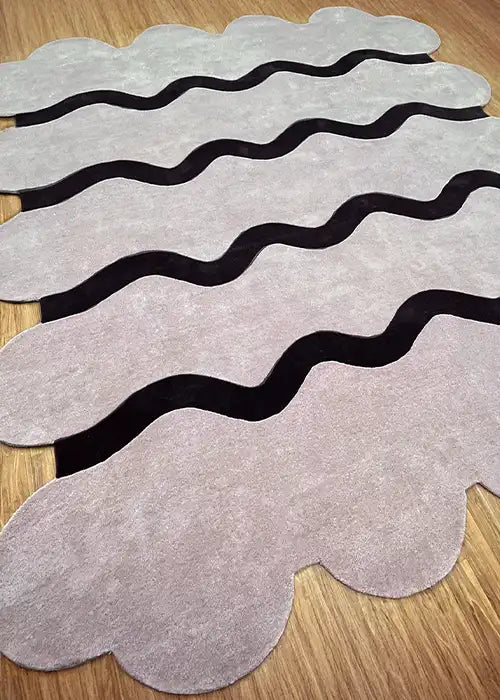 A sculpted edge rug in muted tones with wavy patterns, illuminated by soft natural light on a wooden floor