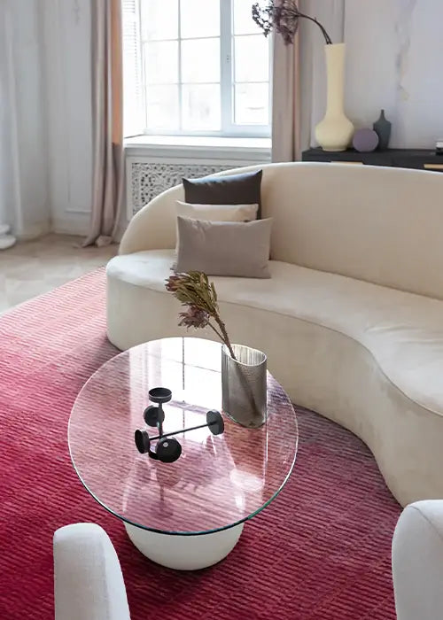 Pink Ombre Loomed Rug in an elegant living room with a curved cream sofa, a glass coffee table, and sculptural decor