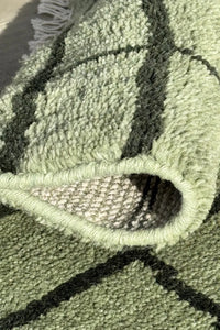 Rectangular hand knotted green wool area rug with a minimalist black grid pattern