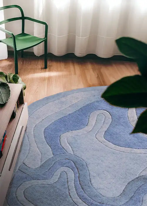 A light blue Rolling Tides rug styled in a bright room with a modern green chair and wooden floors.