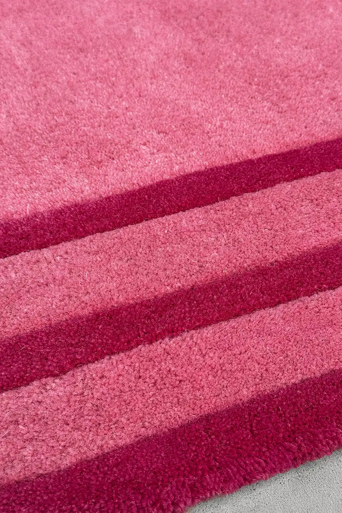 Close-up of tufted pink wool rug with thick stripe detail in rose and fuchsia, hand-carved for texture