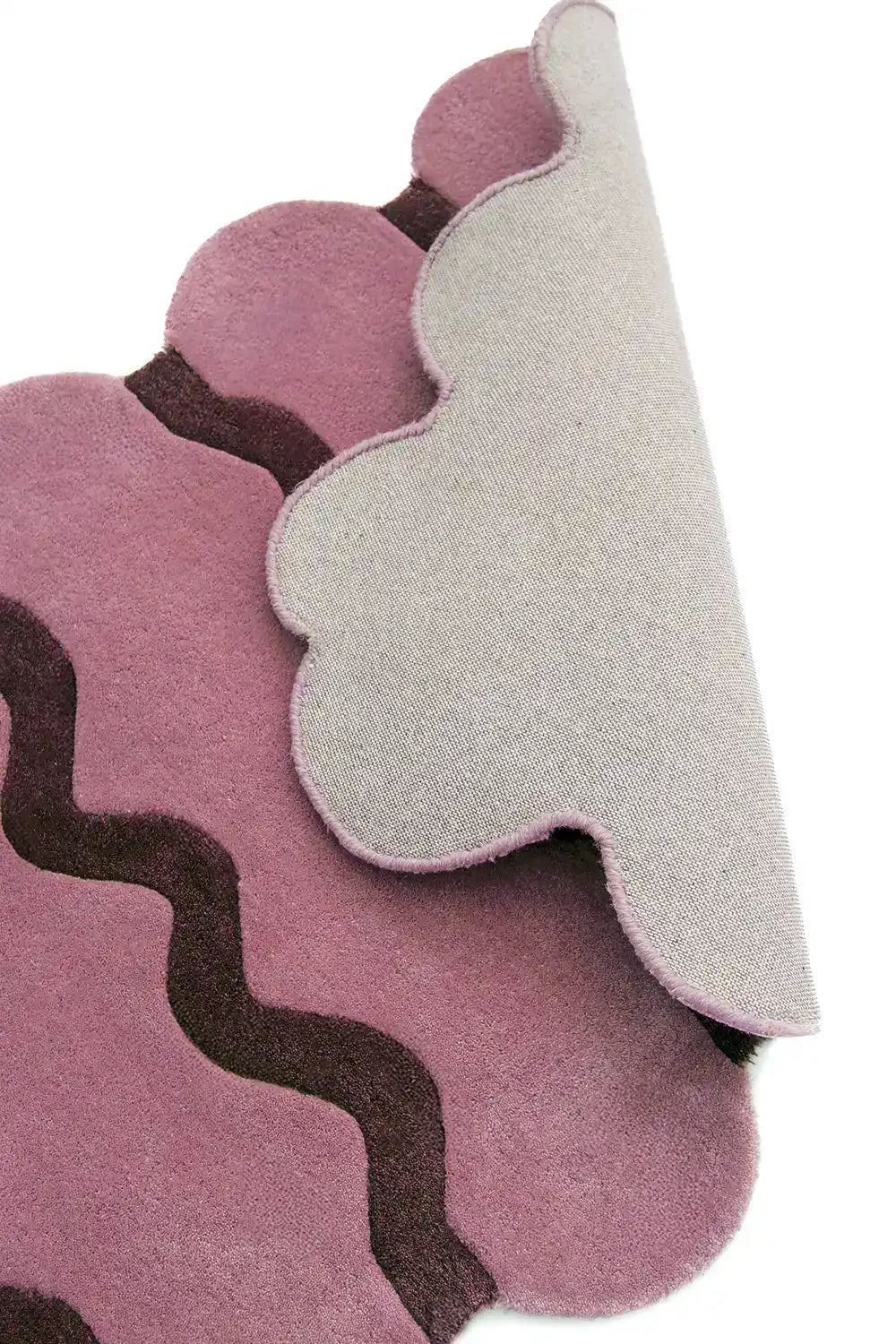 Close-up side view of a rose pink scalloped edge hand-tufted wool rug, showing the detailed texture, backing, and unique scalloped design.