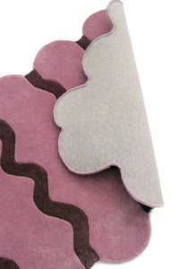 Close-up side view of a rose pink scalloped edge hand-tufted wool rug, showing the detailed texture, backing, and unique scalloped design.