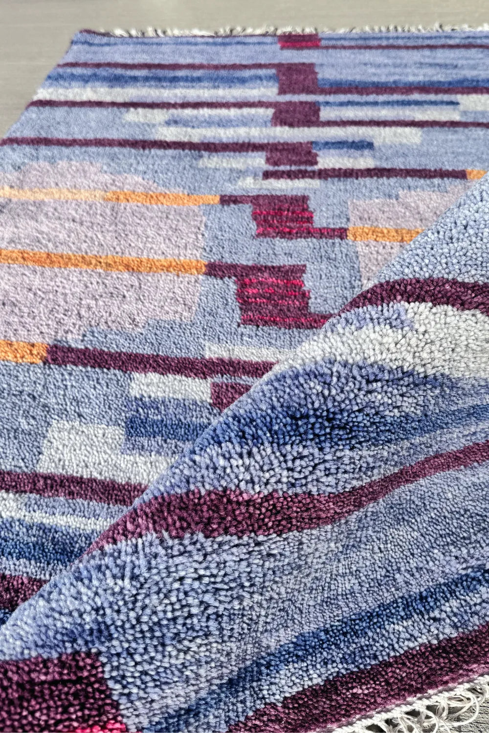 Handmade multicolor wool rug folded to show soft high-pile weave and sculptural carved texture