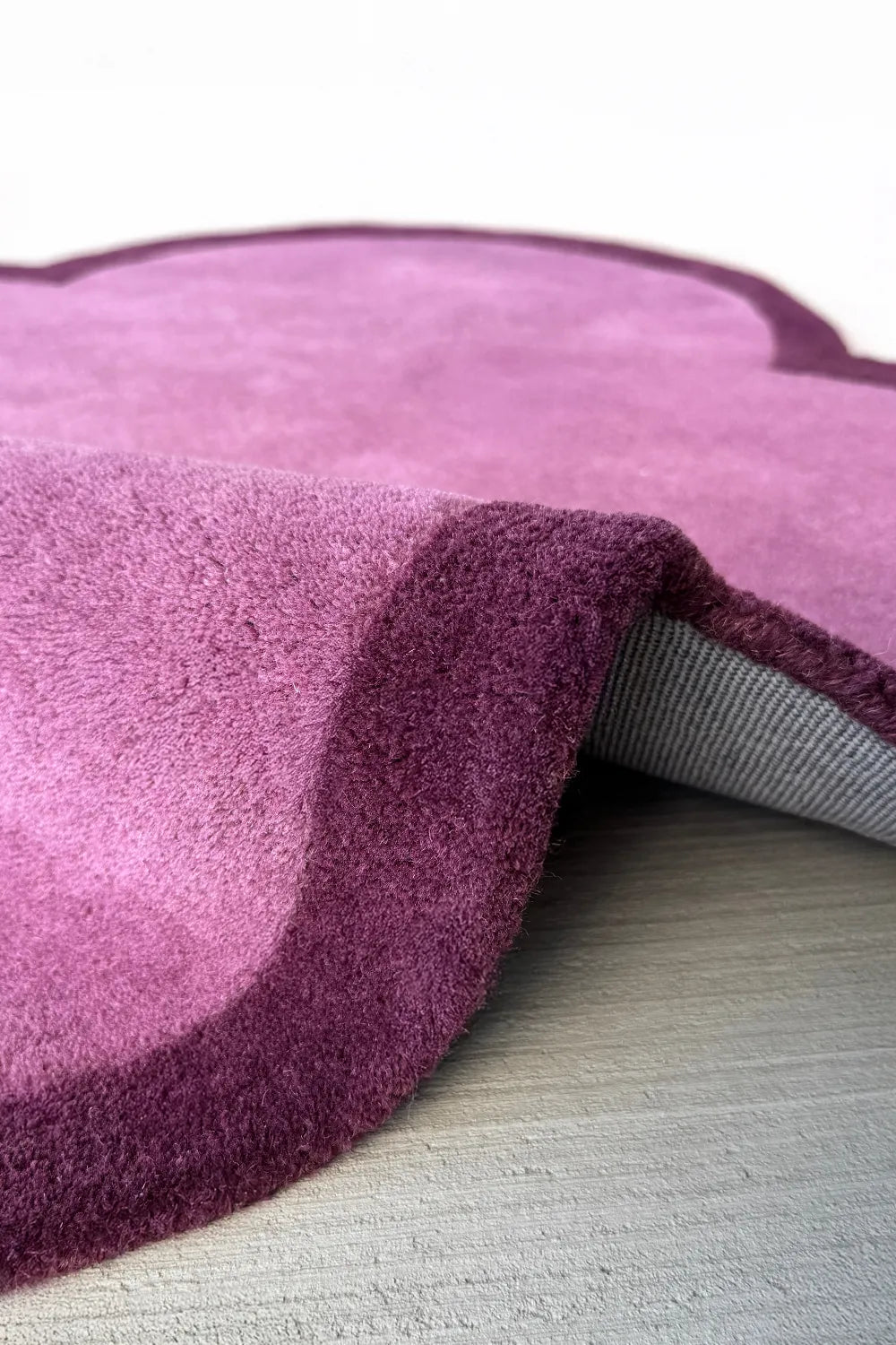 Irregular shaped tufted purple rug with dark border, a unique wool area rug for whimsical or boho interiors