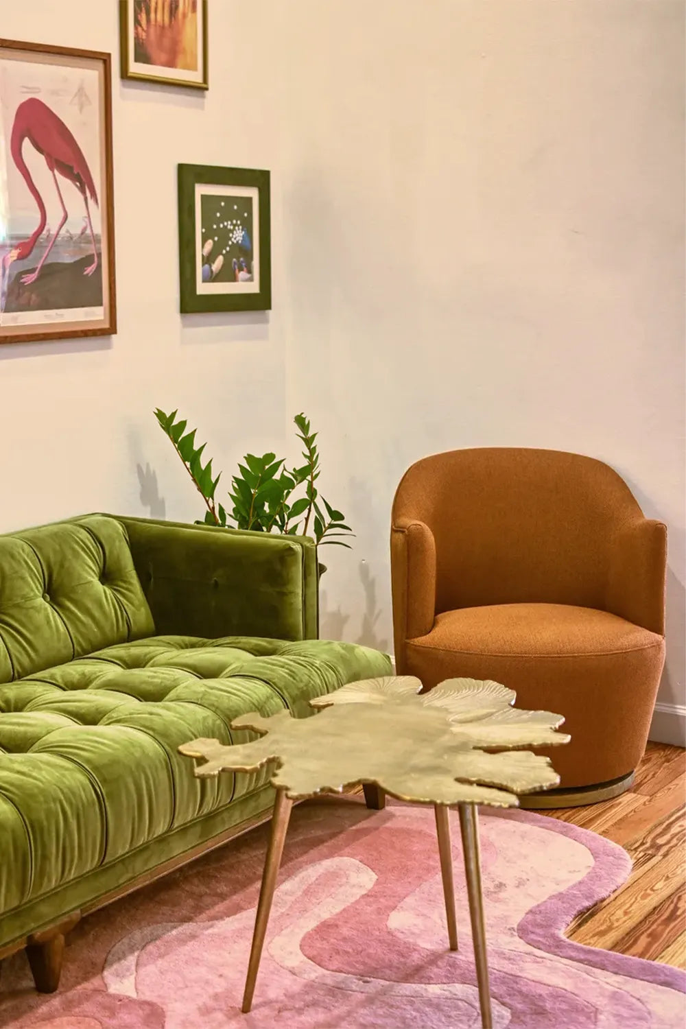 A modern seating area with a green velvet sofa, a rust-orange chair, and a pink Jubi rug, blending mid-century and contemporary styles.