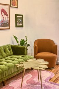A modern seating area with a green velvet sofa, a rust-orange chair, and a pink Jubi rug, blending mid-century and contemporary styles.