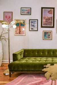 A chic living room featuring a green velvet sofa, a gallery wall of vibrant art, and a pink Jubi rug with wavy patterns, creating a bold yet cozy ambiance.