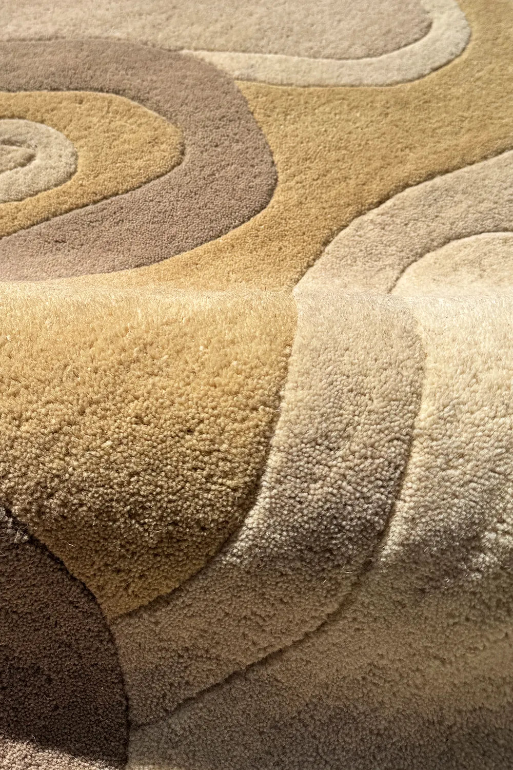 Wavy wool rug with carved details in golden beige and taupe tones
