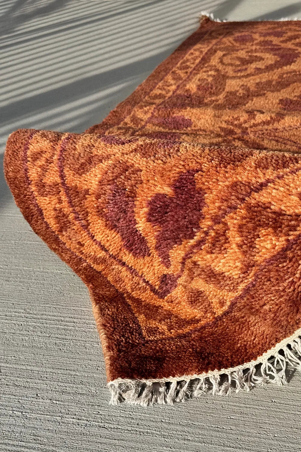 Rust-colored hand-knotted wool rug featuring ornate floral and vine patterns