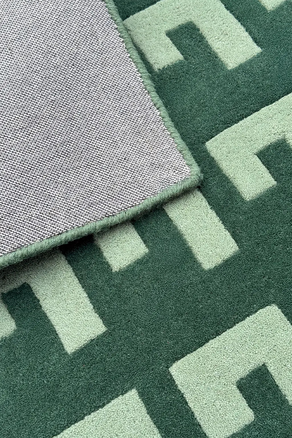 Green geometric rug with soft cotton backing and mint wool pile, shown folded to display structure