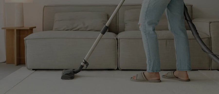 A person vacuuming a light-colored rug in front of a neutral-toned sofa, showcasing easy regular maintenance.