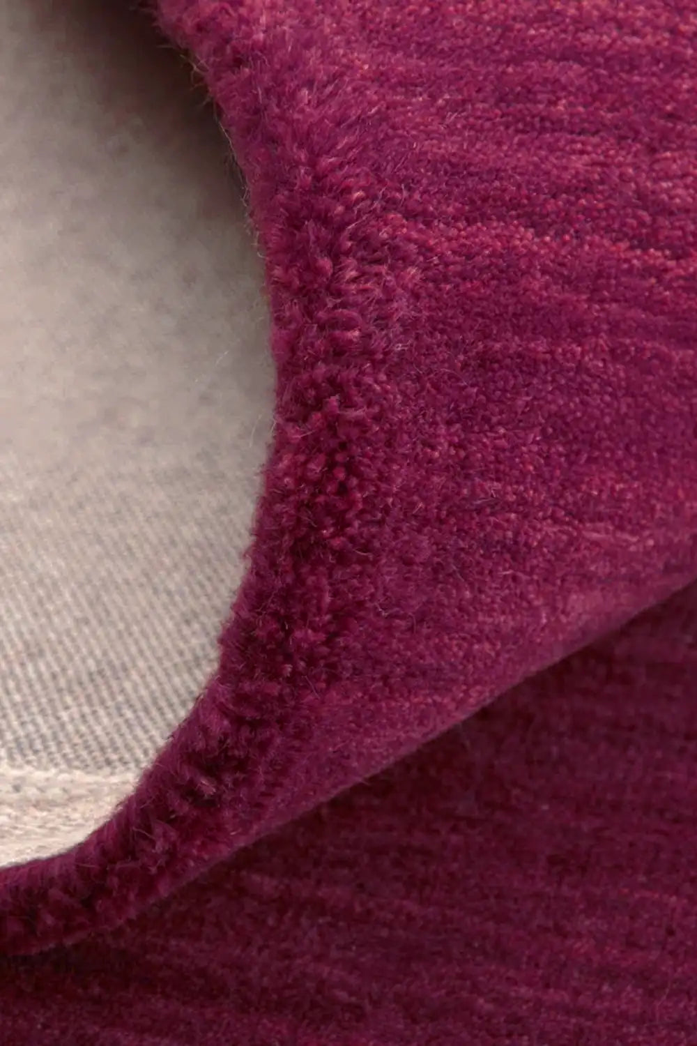Close-up of burgundy round wool rug folded to show cotton backing, plush hand-tufted texture, and dense pile