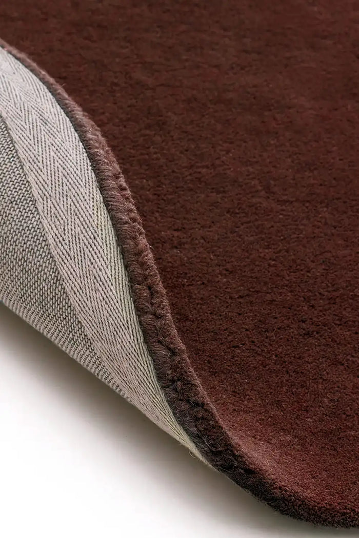 Close-up of hand-tufted brown wool rug with soft pile and stitched edge backing, perfect as a plush area rug