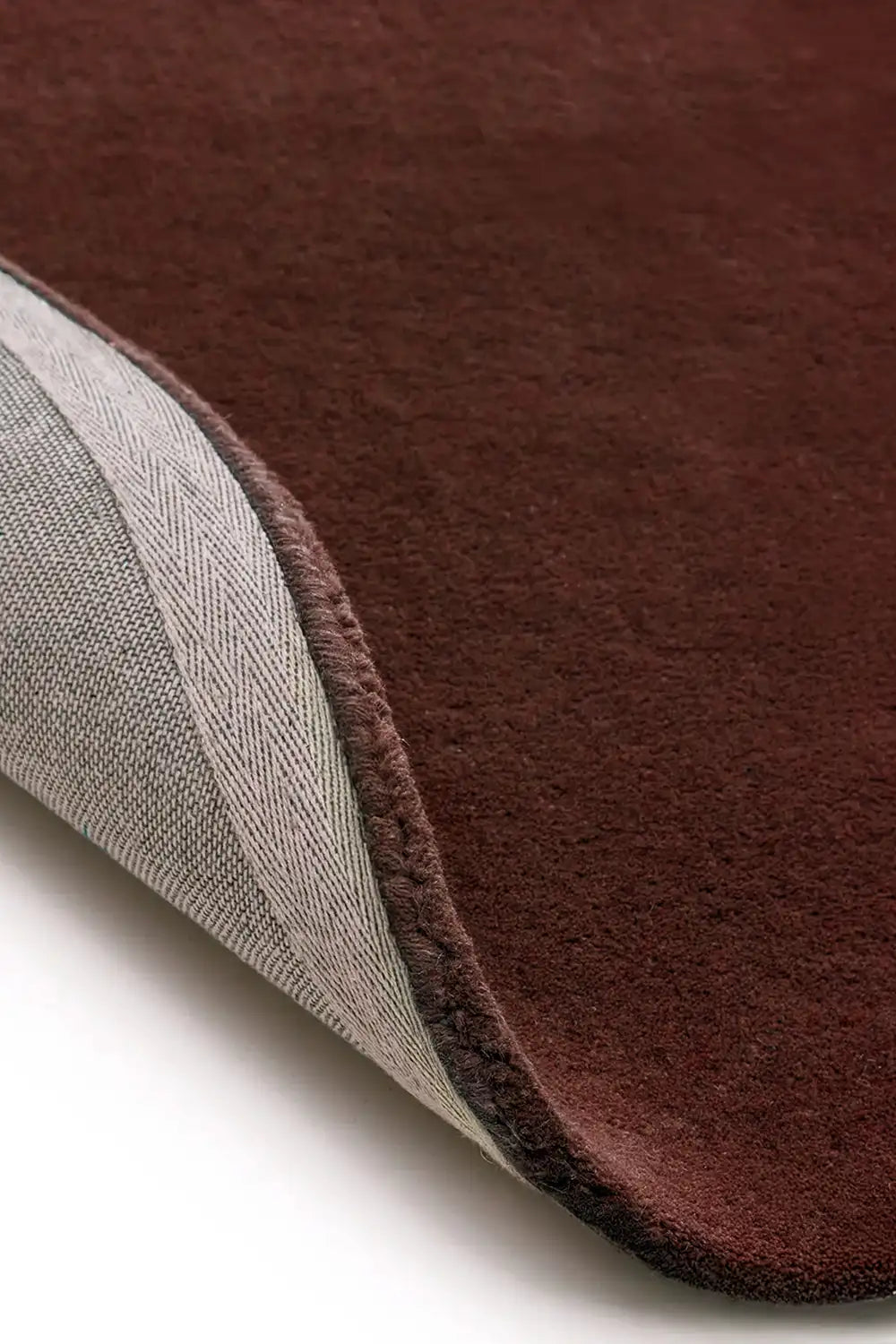 Detail of plush tufted brown wool rug showing curved edge and cotton backing, ideal as a round area rug