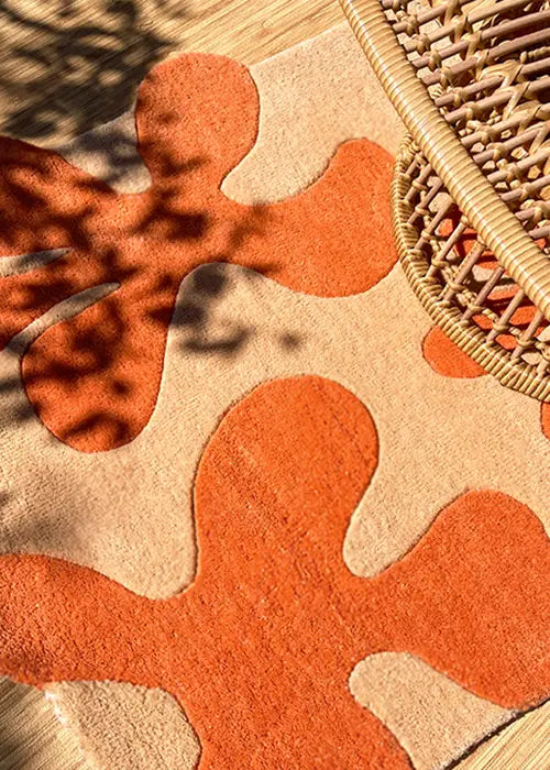 Close-up of an orange and beige abstract wool rug bathed in warm sunlight, highlighting the texture.