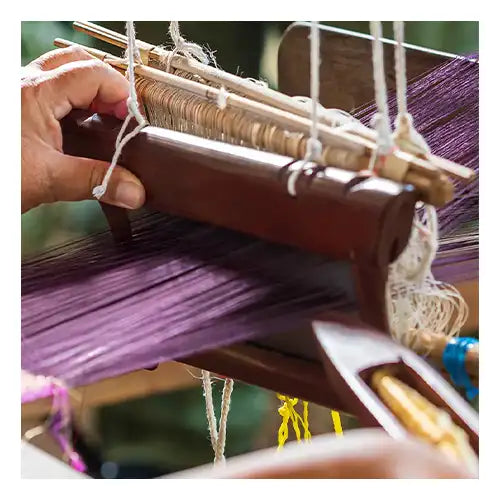 A close-up of a skilled artisan weaving vibrant purple threads on a traditional wooden loom, showcasing the craftsmanship involved in creating handmade rugs.