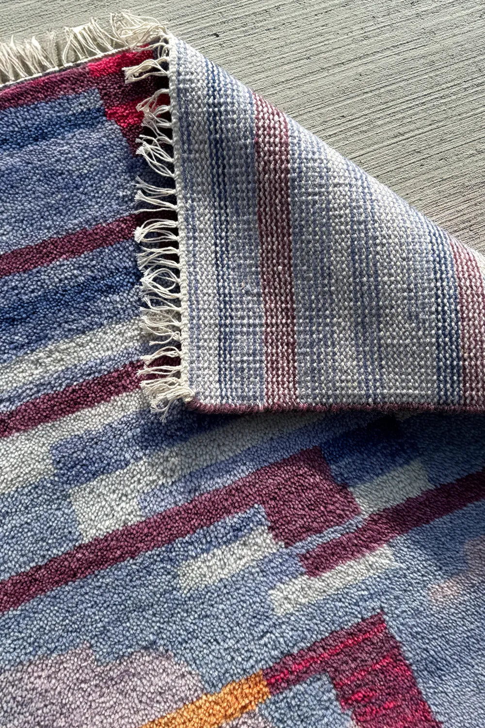 Artisan hand-knotted rug with multicolor stripes, showing woven cotton backing and detailed fringe