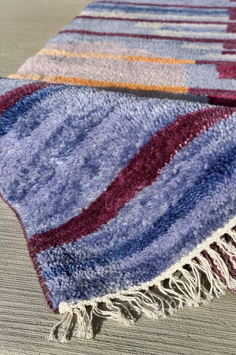 Modern wool area rug in layered shades of blue, gold, and burgundy