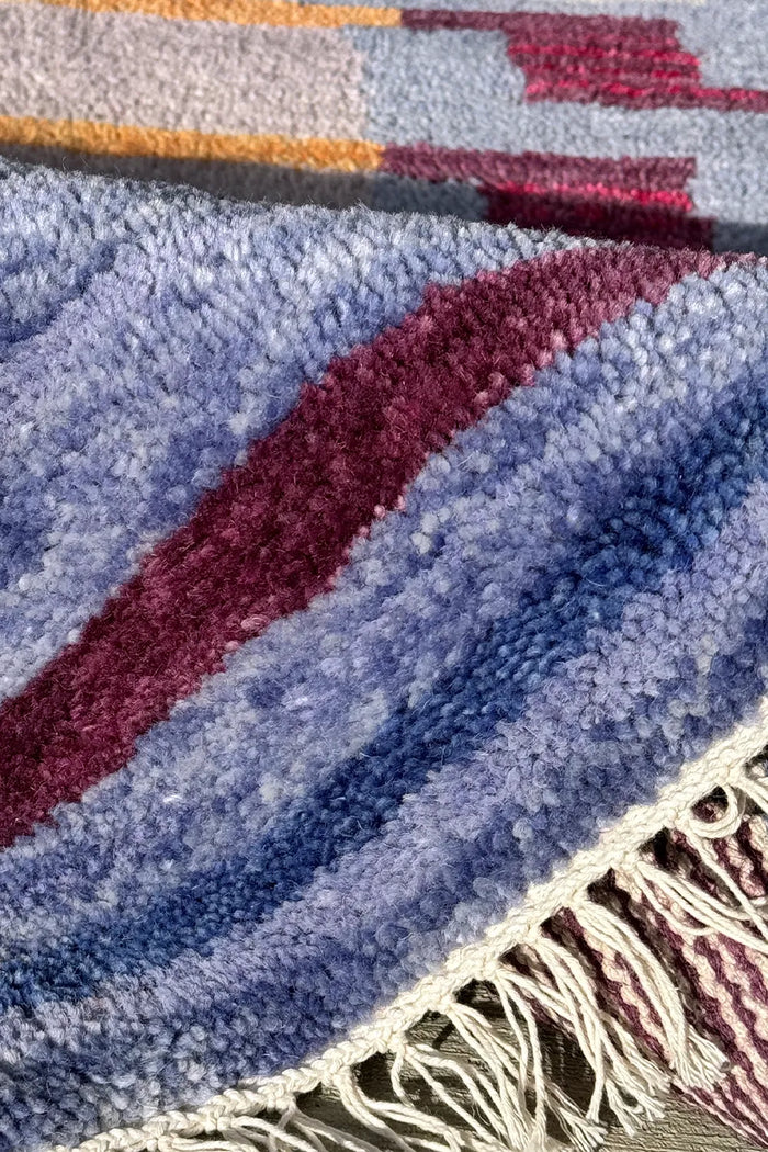 Close-up of hand-knotted wool rug with blue, burgundy, and gold color blocks and fringe edging