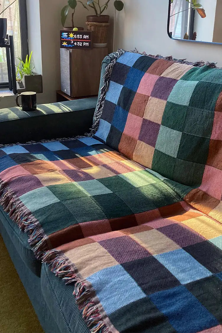 A checkered woven throw blanket in earthy tones draped over a dark green couch, adding warmth and texture to the space.