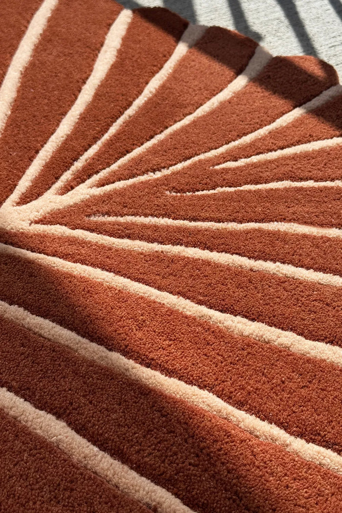 Overhead angle of oval rust rug with carved cream stripes and scalloped edge design