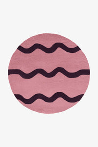 Round pink and purple wool rug with dark scalloped stripes, perfect as a playful accent rug for nursery or kids room