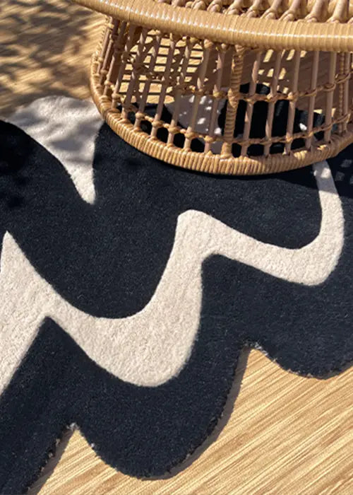 Close-up of a black and white abstract rug under a woven rattan coffee table, showcasing its bold, organic design