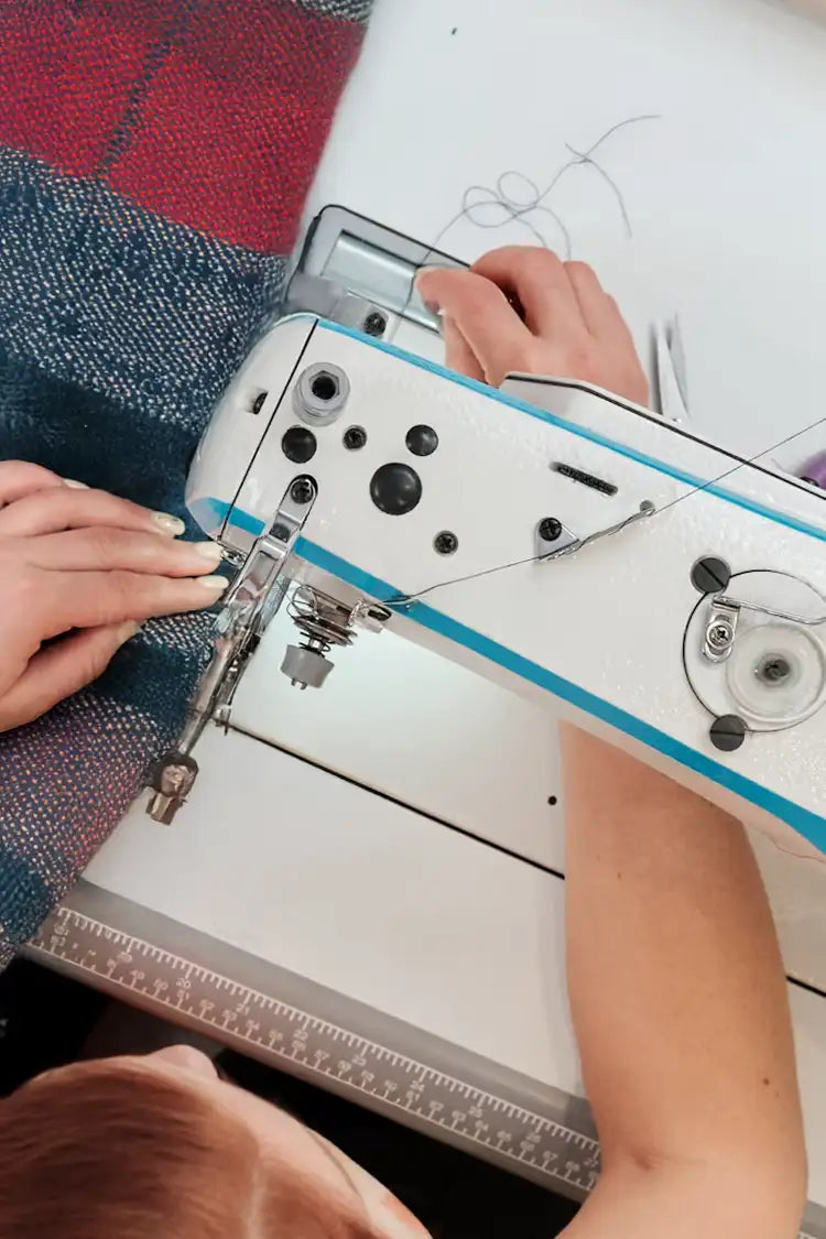 A close-up of an artisan sewing the edges of a woven throw blanket, highlighting expert craftsmanship and attention to detail.