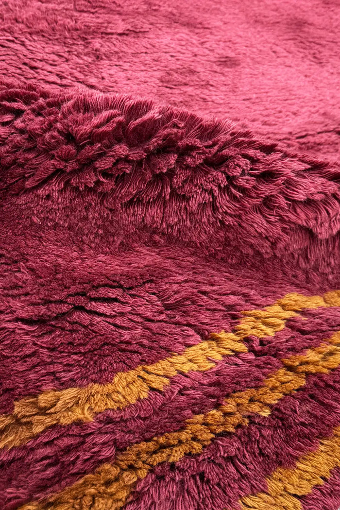 Detail of thick red shag pile with golden yellow stripe, showing soft high-pile texture and handcrafted finish