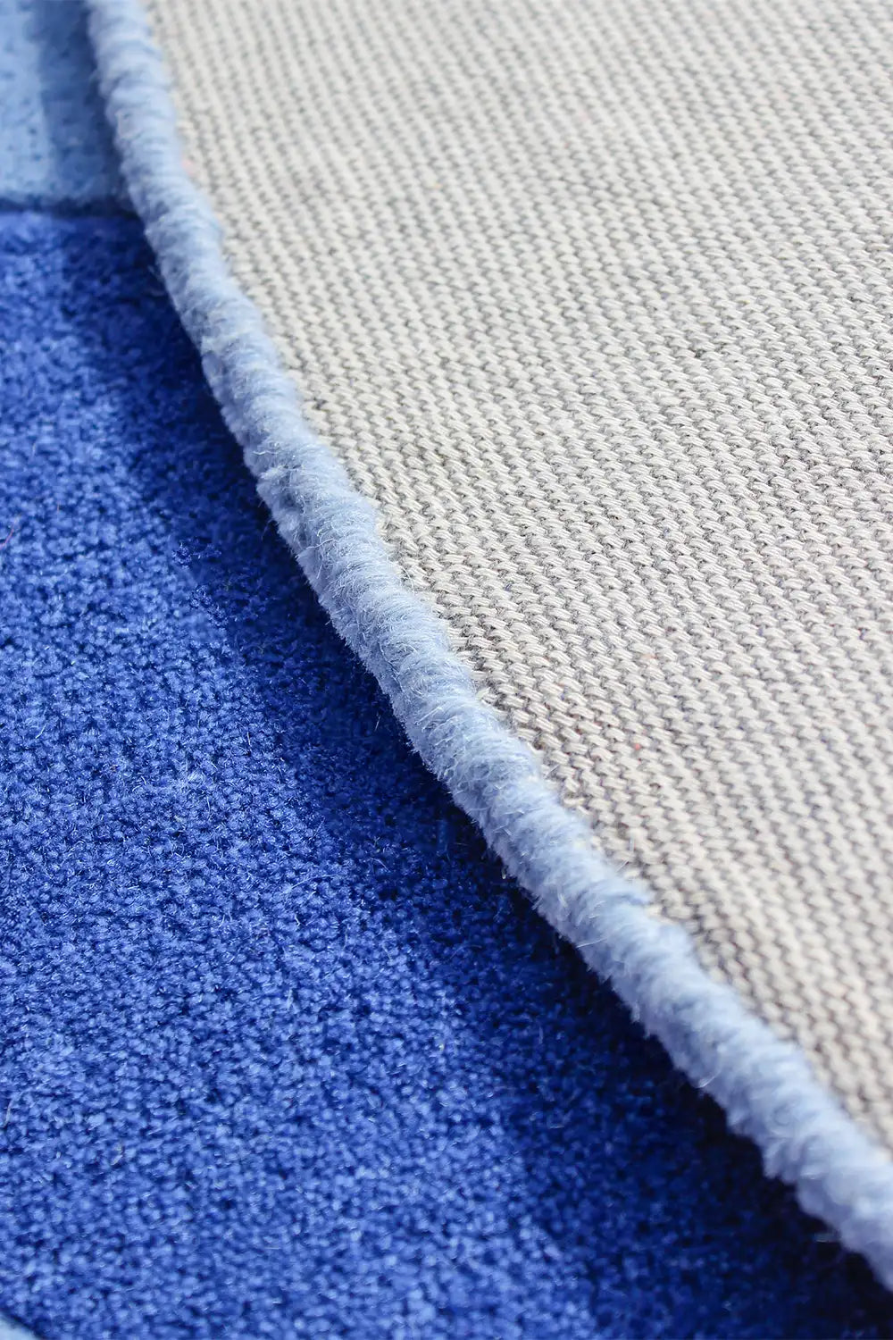 Edge detail of blue irregular shaped wool rug on textured backing