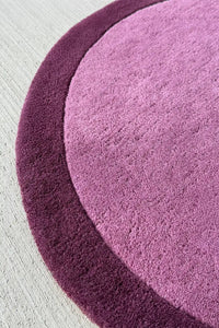 Curved edge of purple irregular shaped round wool rug with a soft plush texture