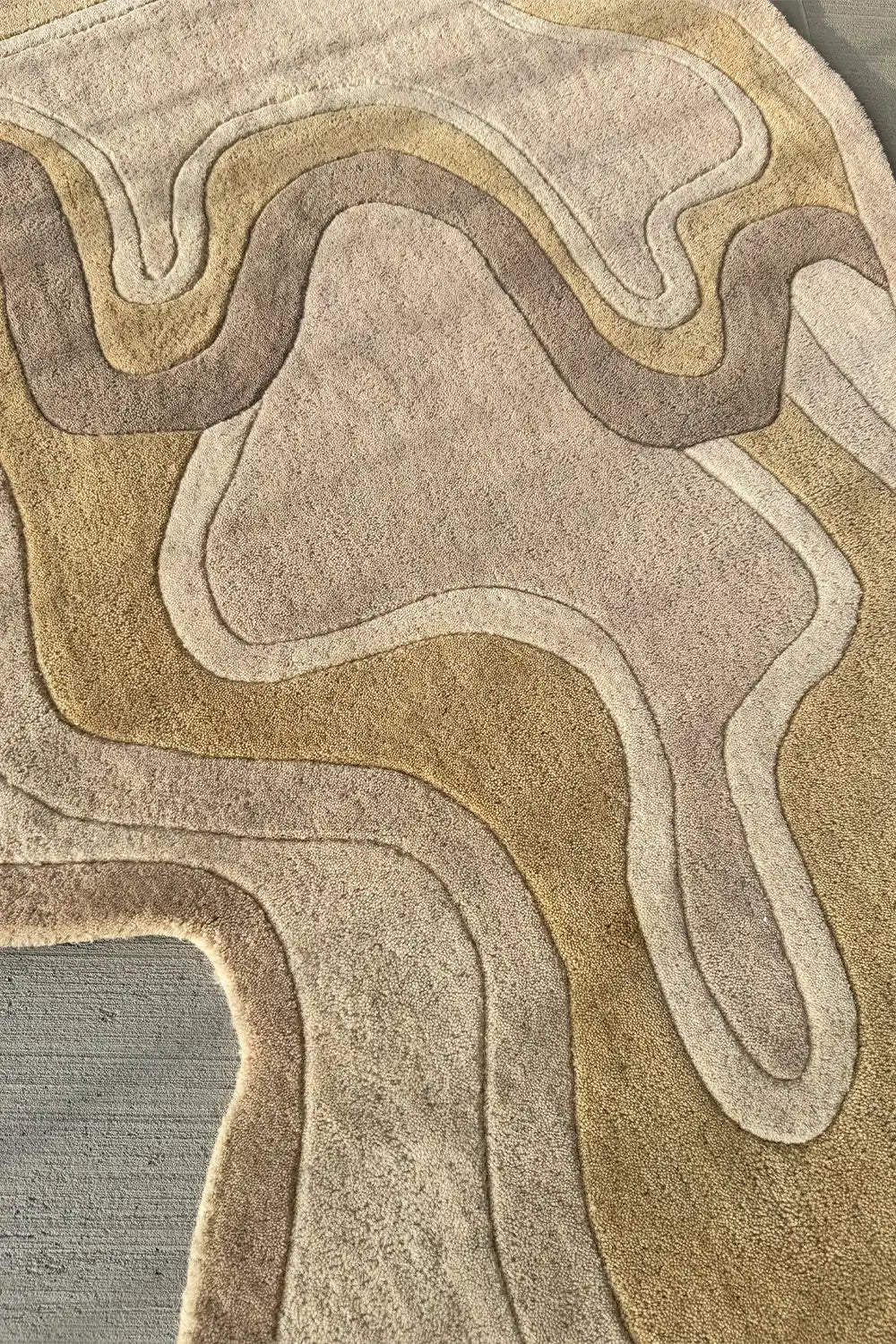 Wavy wool rug with carved details in golden beige and taupe tones
