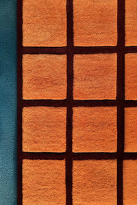 Hand-tufted terracotta wool rug with deep burgundy grid lines and sculpted high-low checkered texture

