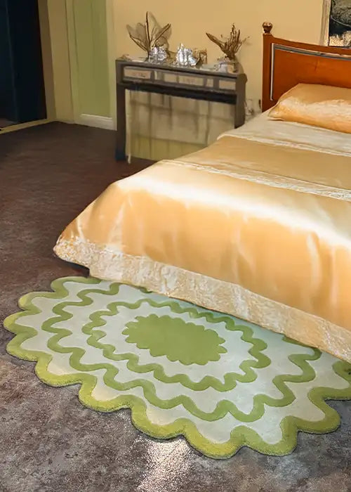 Green scalloped rug placed beside a bed with gold silk bedding, styled in a sophisticated bedroom with a decorative console table