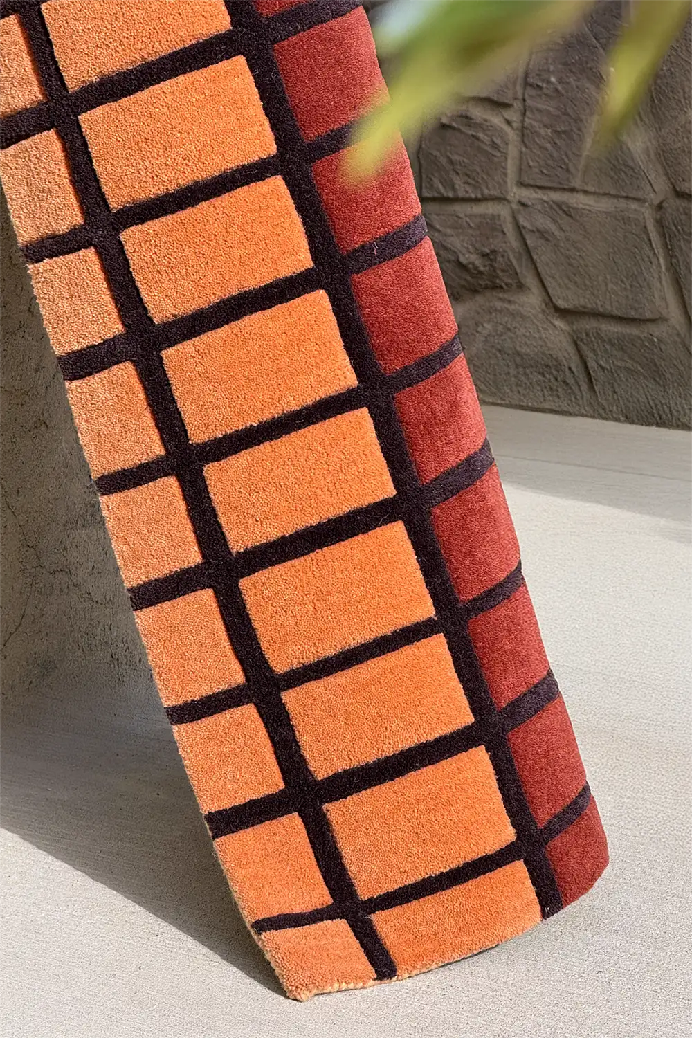 Orange and black checkered wool rug on a stone surface