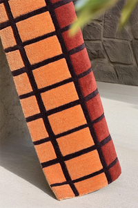 Orange and black checkered wool rug on a stone surface